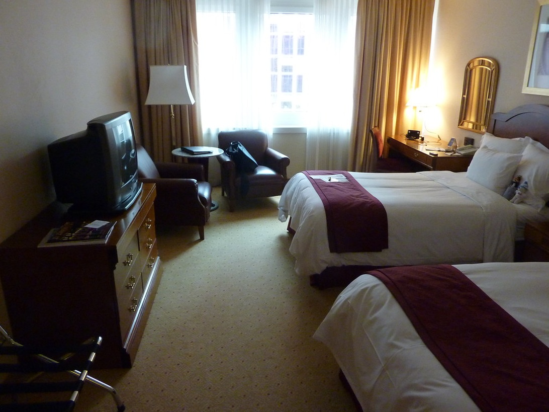 Ein komfortables Hotelzimmer mit zwei Queensize-Betten, weißer Bettwäsche, burgunderroten Läufern, Schreibtisch und Fernseher.